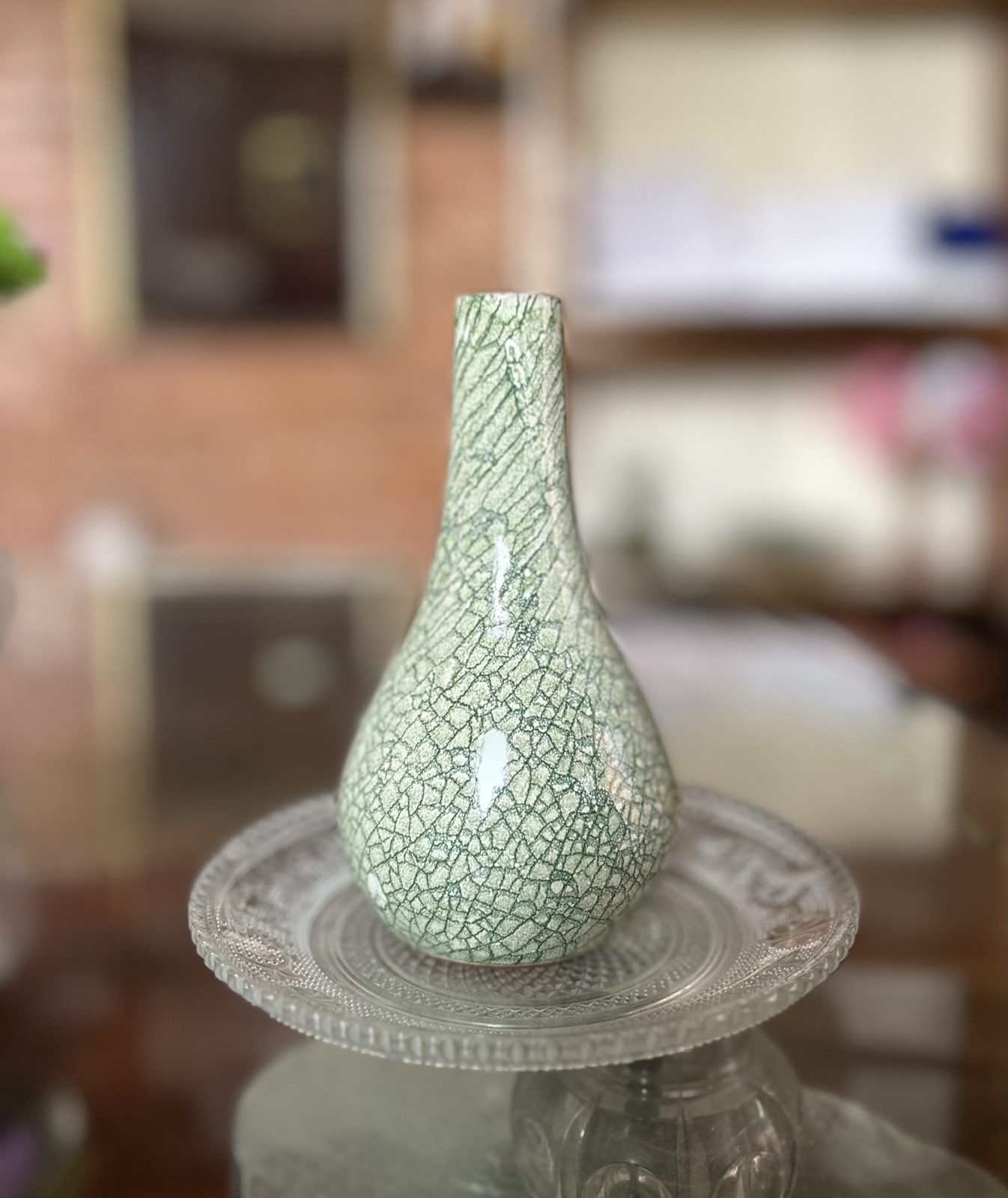 A green crackle-glazed vase on a glass plate
